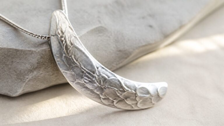 Curved silver pendant detail with subtle raised scale texture