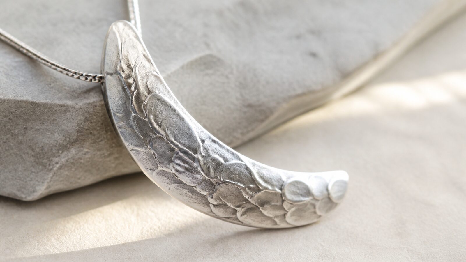 Silver texture in grazing light Curved silver pendant detail with subtle raised scale texture