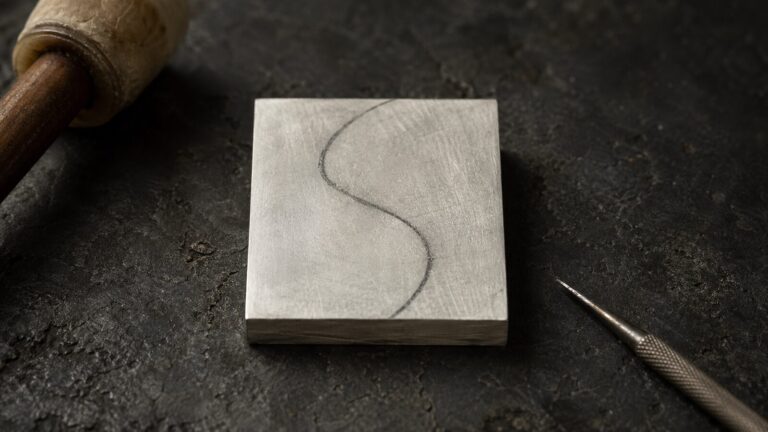 925 silver sheet with charcoal S-curve drafting line on a dark workbench